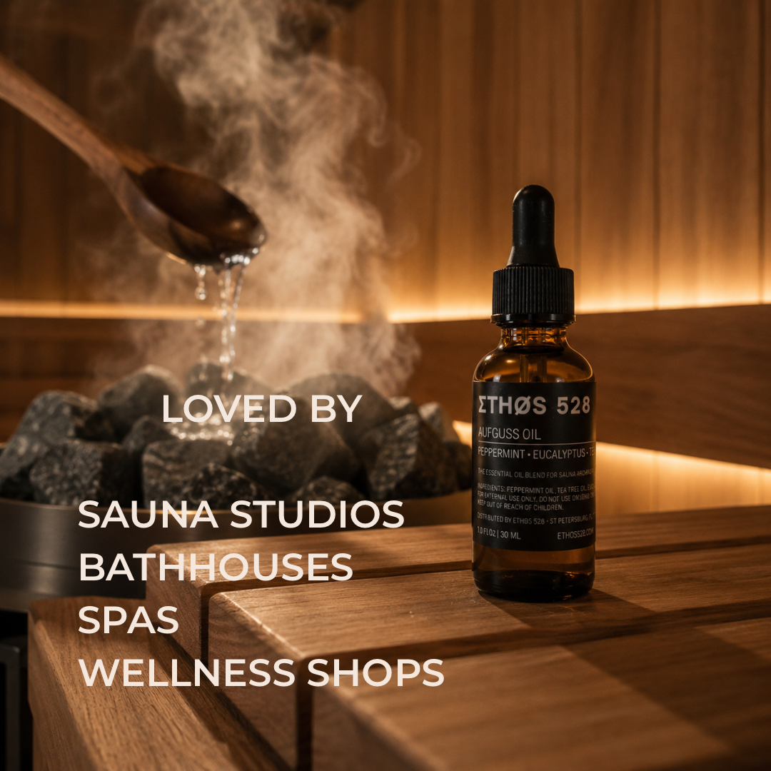A small amber dropper bottle labeled ETHOS 528 AUFGUSS OIL stands on a wooden bench in a sauna with steam rising from dark stones and a wooden spoon pouring water over the sauna rocks. Large overlaid text reads 'LOVED BY SAUNA STUDIOS BATHHOUSES SPAS WELLNESS SHOPS'.