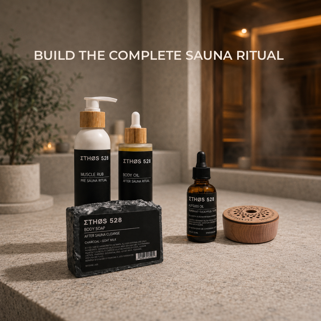 Four Ethos 528 sauna skincare products arranged on a stone surface in a spa-like interior: a body soap bar, a sauna muscle rub pump bottle, a sauna body oil bottle, and an amber aufguss oil bottle, with a wooden sauna essential oil diffuser and steam in the background. White text at the top reads 'BUILD THE COMPLETE SAUNA RITUAL'.